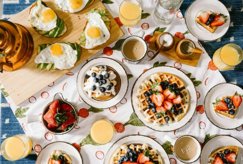 Ontbijttafel met wafels, eieren, fruit en glazen sap.
