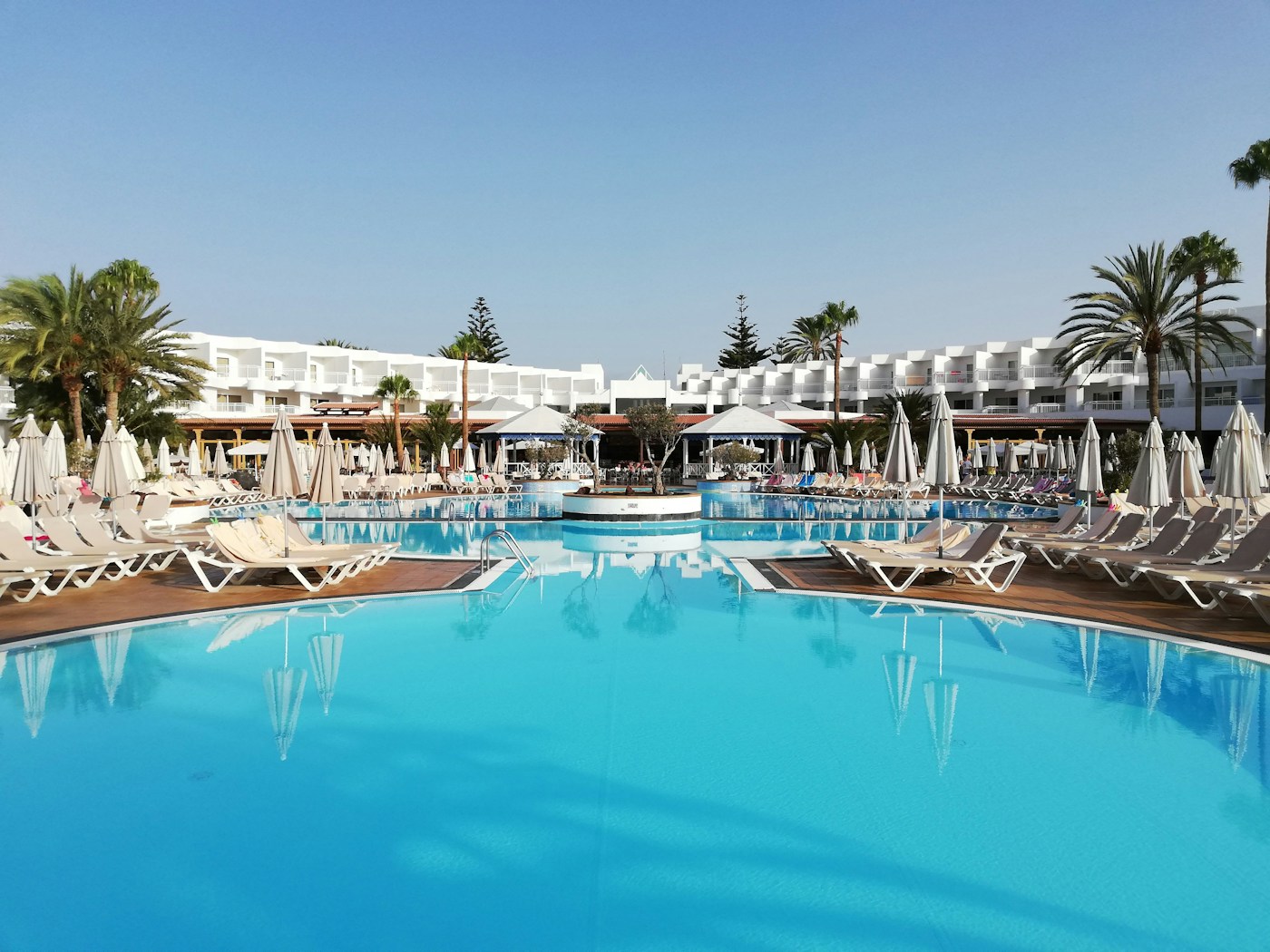 Ligstoelen en palmbomen langs een buitenzwembad bij een resort op Lanzarote.